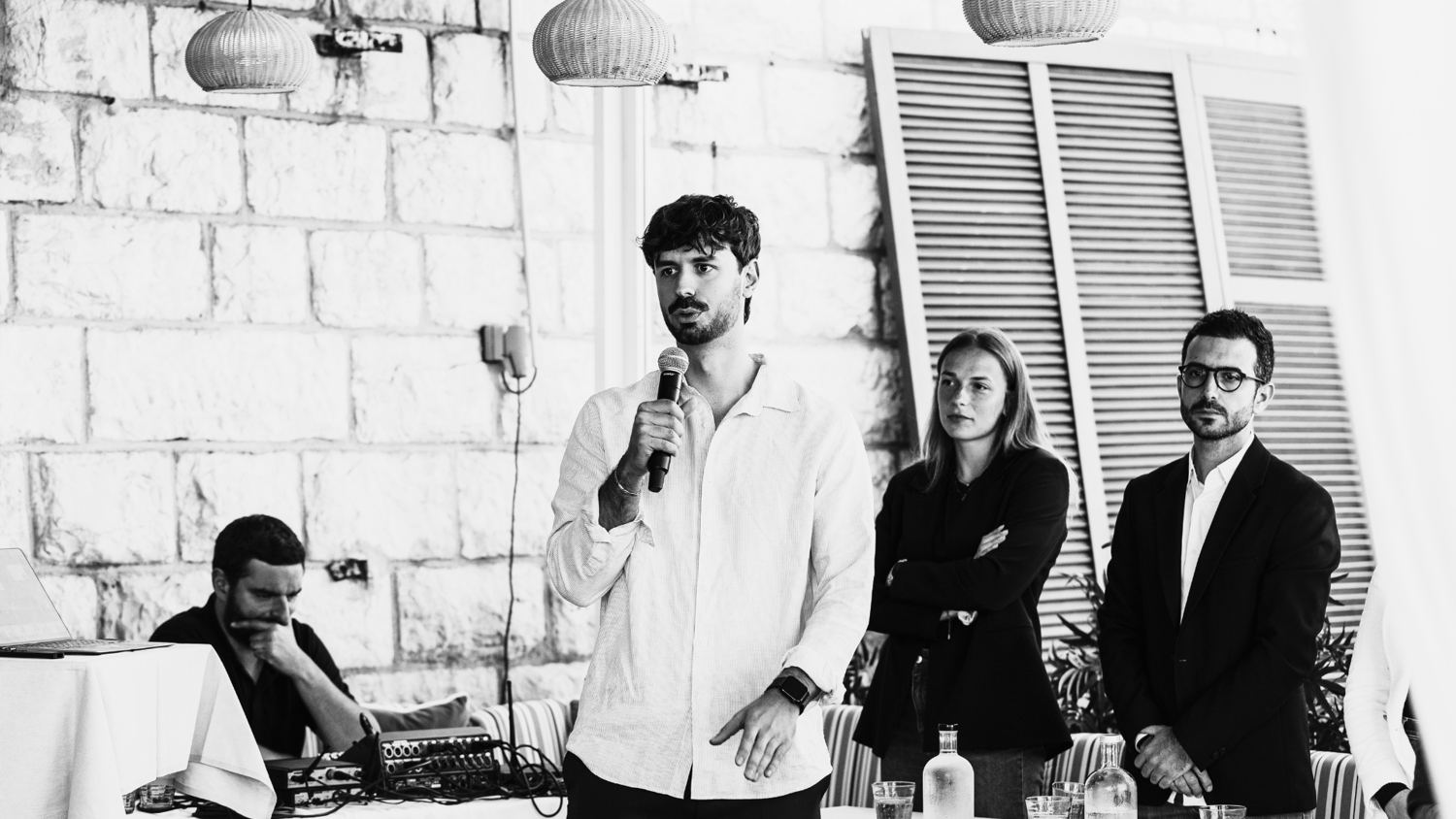 Un intervenant prend la parole au micro devant un public, photo noir et blanc.